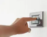 Doigt appuyant sur un interrupteur va et vient ou poussoir, sur un mur texturé.