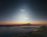 Le ciel étoilé, baigné d'une douce **lumière du jour** naissante, révèle Vénus et Jupiter au-dessus d'une côte rocheuse et d'une mer calme.