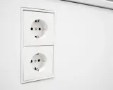 Deux prises EU blanches, alignées verticalement sur un mur blanc. Prêtes à alimenter vos appareils.