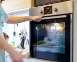Une main ouvre la porte d'un four moderne. L'ampérage du four est réglé pour une cuisson parfaite.
