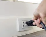 Main d'une personne branchant un appareil sur une prise murale. Une solution simple pour installer une prise électrique sans percer.