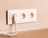 Prise électrique blanche avec un câble branché, installée à la hauteur du plan de travail.