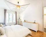 Éclairage chambre : suspension design en bois, lampe sur trépied et commode blanche dans une chambre moderne.