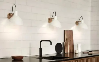 Trois appliques murales blanches avec un bras noir et une base dorée, éclairant un mur de carreaux blancs. Le branchement applique murale avec interrupteur est discret.