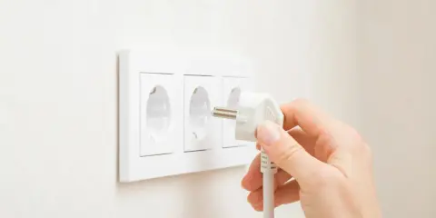 Main d'une personne branchant une prise électrique dans une prise murale triple.