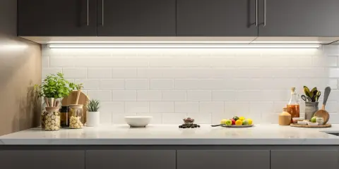 Éclairage subtil sous les armoires sombres, mettant en valeur le carrelage blanc et les objets décoratifs. Une **reglette LED design** illumine la cuisine.