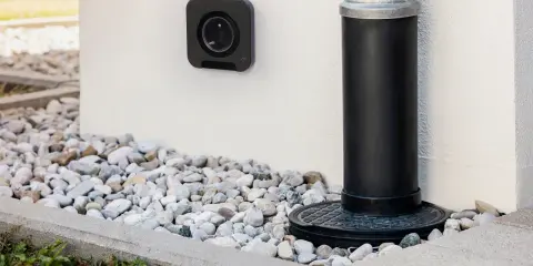 Une prise femelle étanche noire est fixée au mur blanc, à côté d'une descente d'eau.