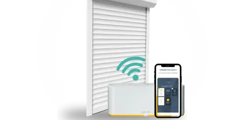 Un volet roulant blanc connecté, une box domotique Somfy et un smartphone affichant l'application. Idéal pour savoir quel volet roulant choisir.