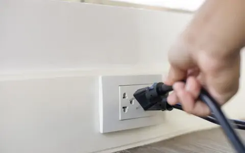 Main d'une personne branchant un appareil sur une prise murale. Une solution simple pour installer une prise électrique sans percer.