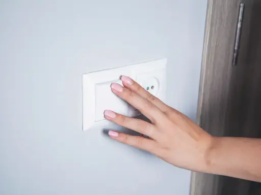 Main d'une femme aux ongles roses actionnant un interrupteur blanc, prêt pour le branchement d'une lampe de chevet.