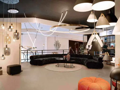 Un salon moderne avec un canapé incurvé noir, des tables basses, un tapis rond et une variété d'ampoules design suspendues au plafond.