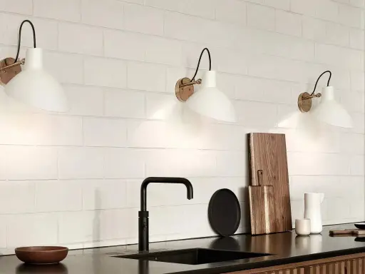 Trois appliques murales blanches avec un bras noir et une base dorée, éclairant un mur de carreaux blancs. Le branchement applique murale avec interrupteur est discret.