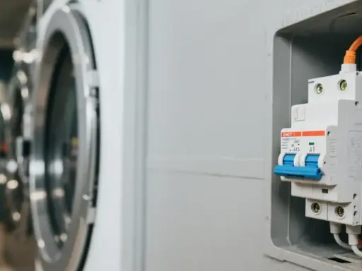 Disjoncteur machine à laver, prêt à protéger l'appareil. L'image montre un disjoncteur blanc et bleu, avec des fils orange et jaunes connectés, à côté d'une machine à laver.