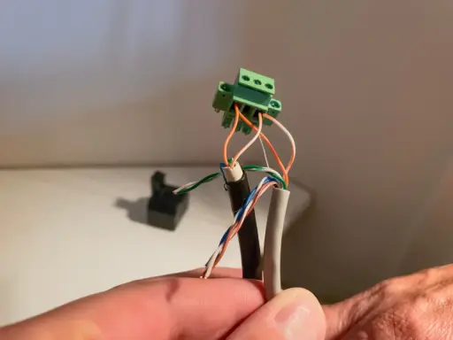 Connexion de fils électriques colorés à un connecteur vert. Un petit point lumineux attire l'œil sur le fil blanc.