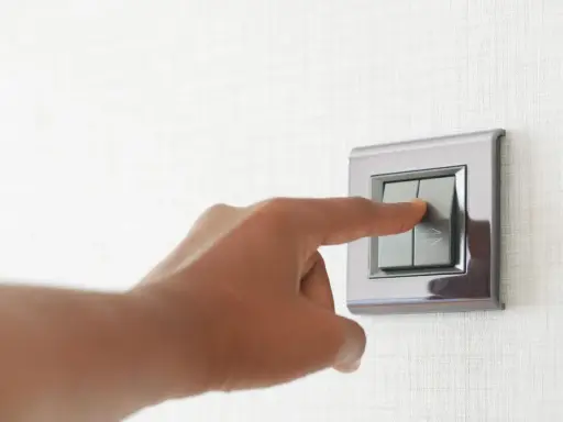 Doigt appuyant sur un interrupteur va et vient ou poussoir, sur un mur texturé.
