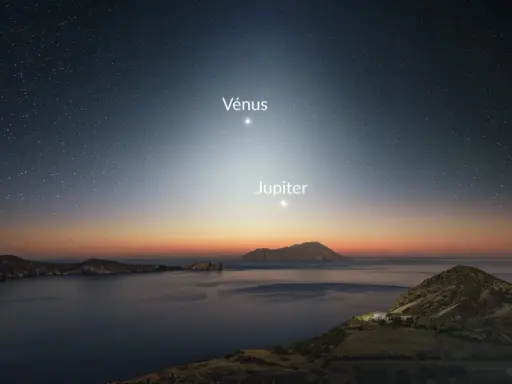 Le ciel étoilé, baigné d'une douce **lumière du jour** naissante, révèle Vénus et Jupiter au-dessus d'une côte rocheuse et d'une mer calme.