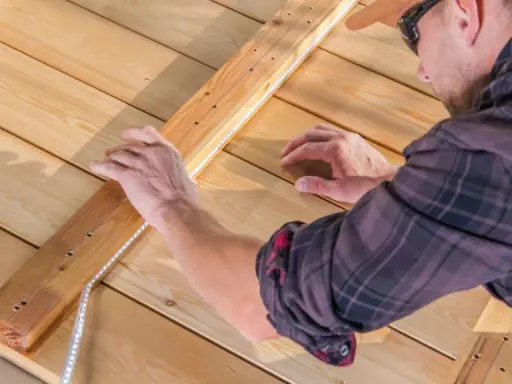 Un homme installe un ruban LED sur une structure en bois. Il réfléchit à quel ruban LED choisir pour son projet d'éclairage extérieur.