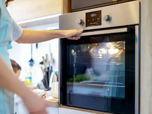 Une main ouvre la porte d'un four moderne. L'ampérage du four est réglé pour une cuisson parfaite.