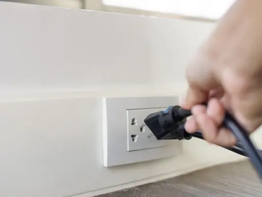 Main d'une personne branchant un appareil sur une prise murale. Une solution simple pour installer une prise électrique sans percer.