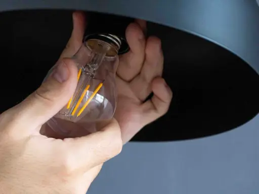 Mains tenant une ampoule LED à filament, prête à être installée. La chaleur de l'ampoule est symbolisée par ses filaments jaunes lumineux.