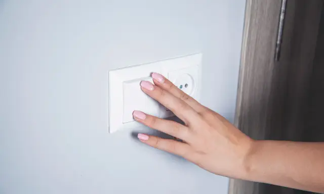 Main d'une femme aux ongles roses actionnant un interrupteur blanc, prêt pour le branchement d'une lampe de chevet.