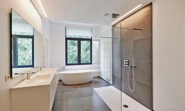 Salle de bain moderne avec baignoire îlot, double vasque et douche à l'italienne. L'éclairage intégré en hauteur applique une ambiance douce.