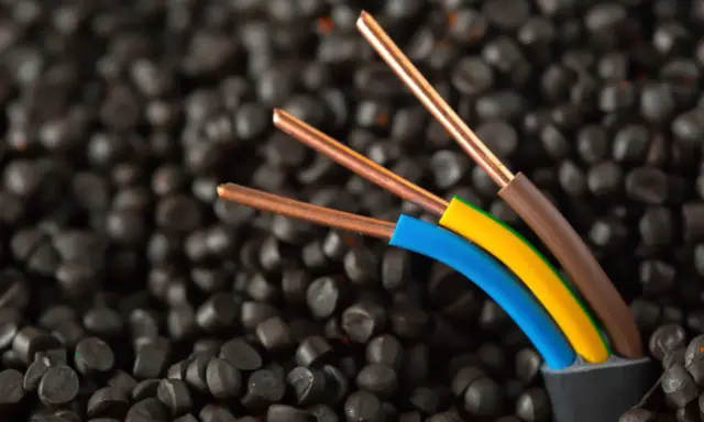 Trois fils électriques aux conducteurs en cuivre, dont un fil marron électrique, sortent d'un câble noir sur un fond de granulés noirs.