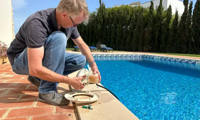 Homme près d'une piscine, tenant une pièce de la pompe. Il vérifie le disjoncteur pompe piscine pour s'assurer que tout fonctionne.
