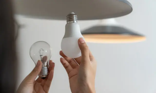 Une ampoule sans électricité, une ampoule LED moderne et une main tenant les deux, prête à remplacer l'ancienne.
