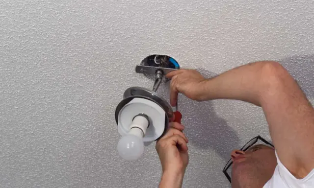 Un homme installe un luminaire au plafond avec un tournevis.