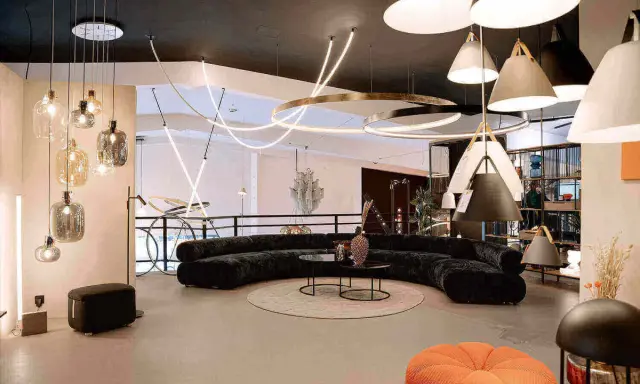 Un salon moderne avec un canapé incurvé noir, des tables basses, un tapis rond et une variété d'ampoules design suspendues au plafond.