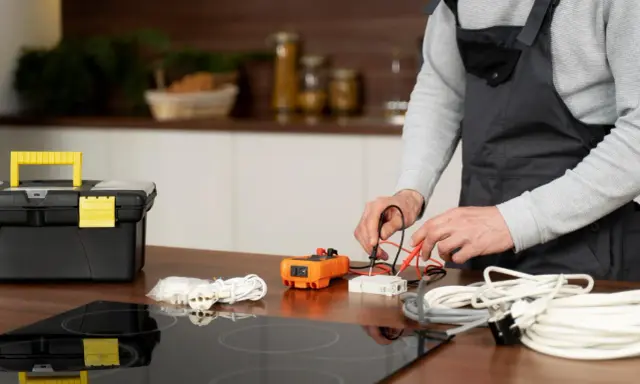 Un technicien vérifie un fusible pour plaque induction avec un multimètre. Outils et câbles à proximité.