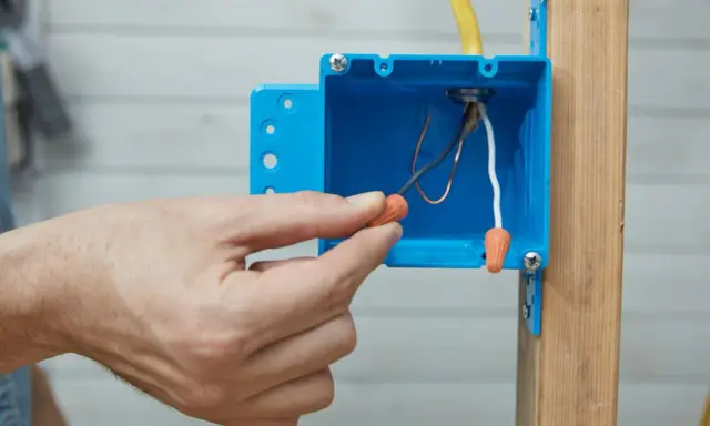 Main tenant utilise un connecteur pour condamner une prise électrique. Les fils électriques sont visibles dans la boîte bleue.