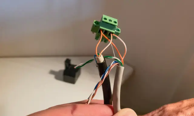Connexion de fils électriques colorés à un connecteur vert. Un petit point lumineux attire l'œil sur le fil blanc.