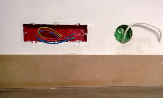 Boîtier rouge avec fils électriques colorés, prêt pour un interrupteur compteur électrique. Une boîte verte avec un câble blanc est visible à droite.