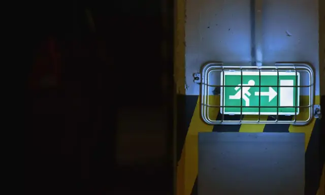 Panneau de sortie de secours vert lumineux, indiquant la direction à suivre. Le **baes signification** est claire : sécurité et évacuation.