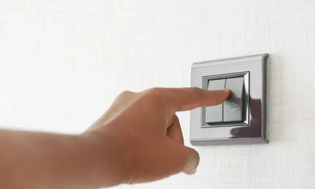 Doigt appuyant sur un interrupteur va et vient ou poussoir, sur un mur texturé.
