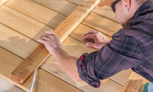 Un homme installe un ruban LED sur une structure en bois. Il réfléchit à quel ruban LED choisir pour son projet d'éclairage extérieur.