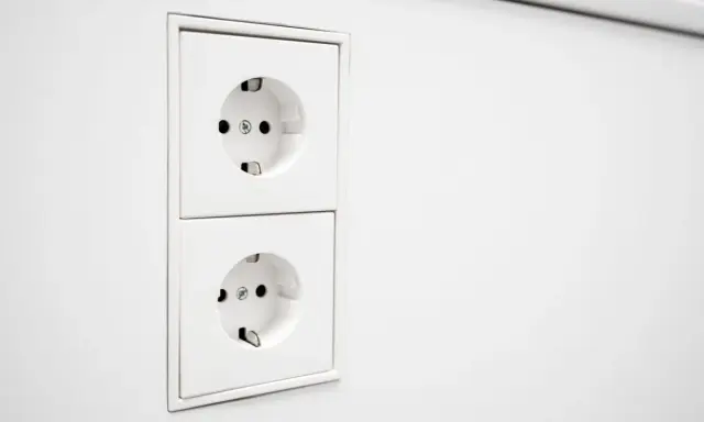 Deux prises EU blanches, alignées verticalement sur un mur blanc. Prêtes à alimenter vos appareils.