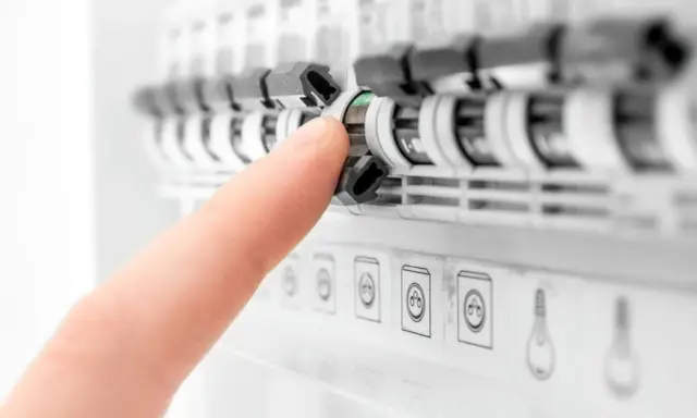 Doigt actionnant un disjoncteur dans un tableau électrique. Aide à comprendre quel disjoncteur différentiel choisir pour votre installation.