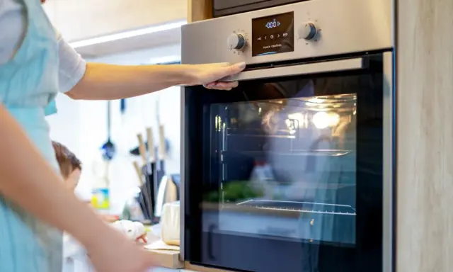 Une main ouvre la porte d'un four moderne. L'ampérage du four est réglé pour une cuisson parfaite.