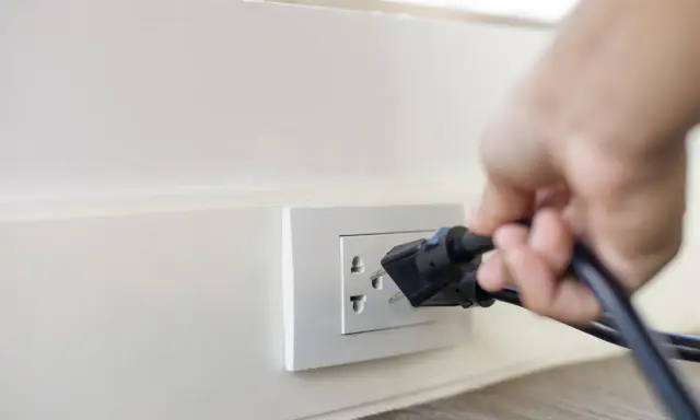 Main d'une personne branchant un appareil sur une prise murale. Une solution simple pour installer une prise électrique sans percer.
