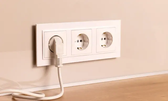 Prise électrique blanche avec un câble branché, installée à la hauteur du plan de travail.