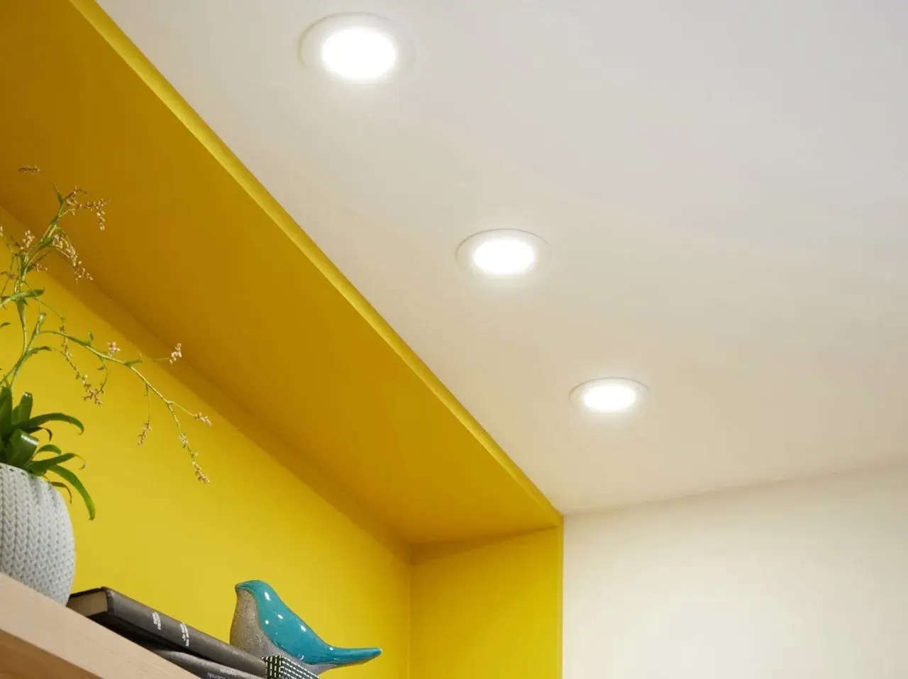 Trois spots lumineux éclairent un plafond blanc au-dessus d'une étagère jaune vif.