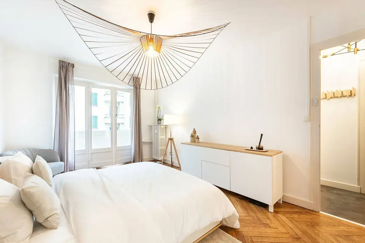 Éclairage chambre : suspension design en bois, lampe sur trépied et commode blanche dans une chambre moderne.