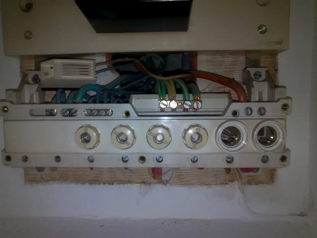 Vue rapprochée d'un tableau électrique avec des fils et des fusibles. Un fusible semble surchauffer, signalant un problème potentiel.