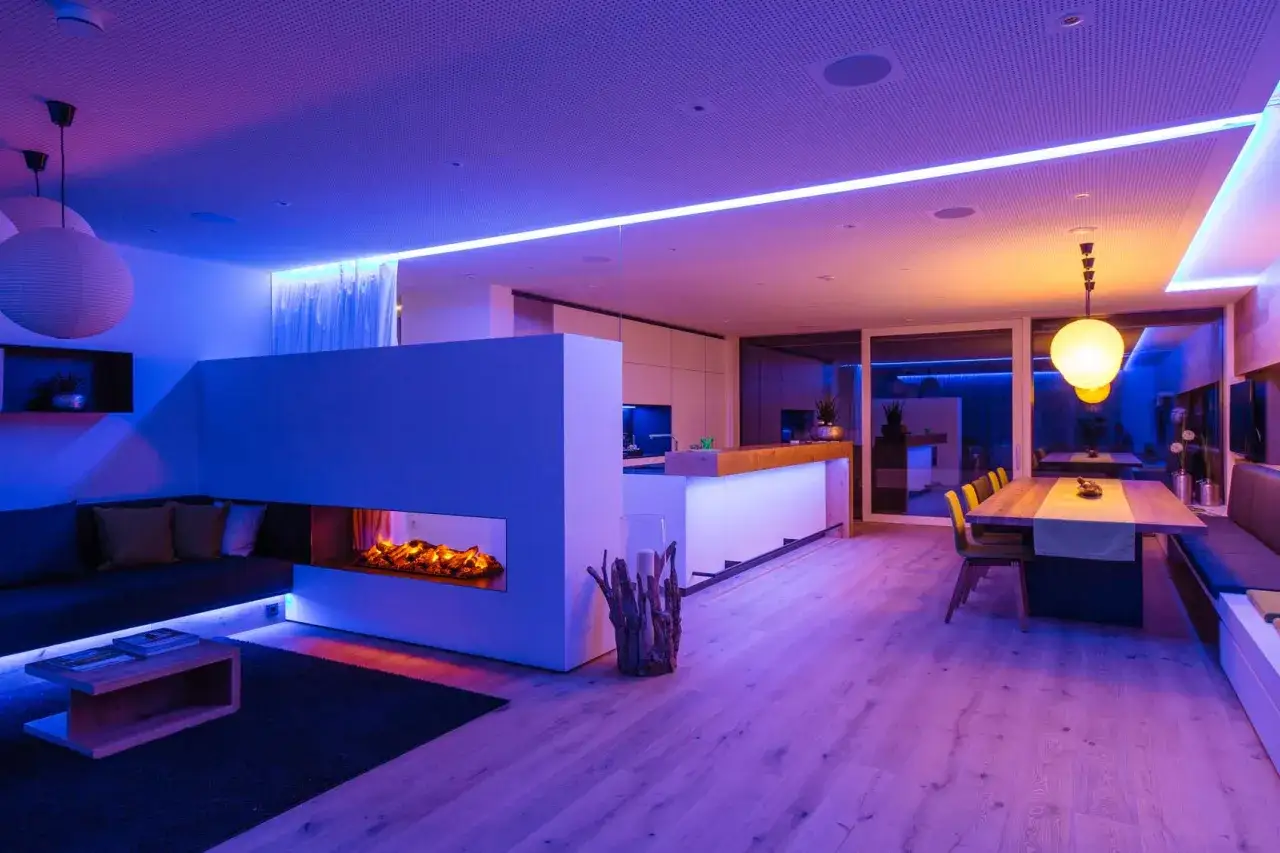Salon moderne avec chemin&eacute;e, canap&eacute;, table et cuisine. L'ampoule du salon diffuse une lumi&egrave;re d'ambiance color&eacute;e.