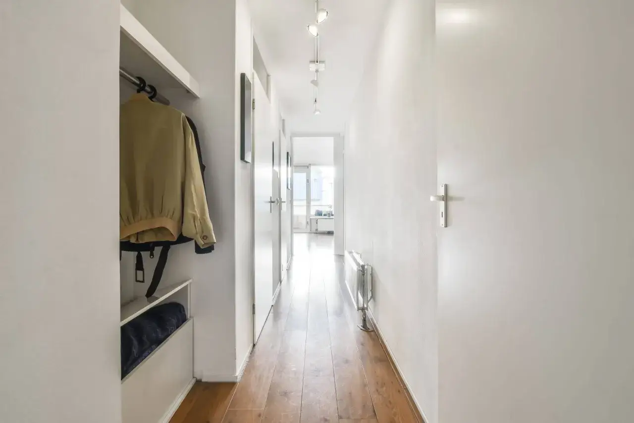 Éclairage d'un long et étroit couloir avec des portes blanches, un radiateur et un vestiaire.