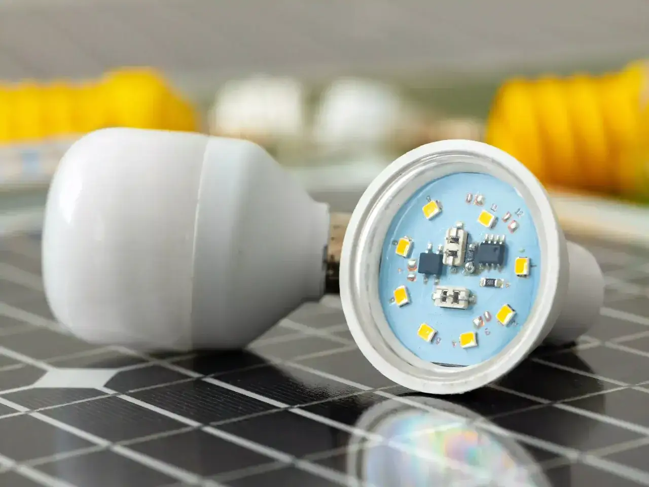 Comment reconnaître une ampoule LED : une ampoule blanche ouverte révèle ses puces lumineuses sur un fond bleu, posée sur un panneau solaire.
