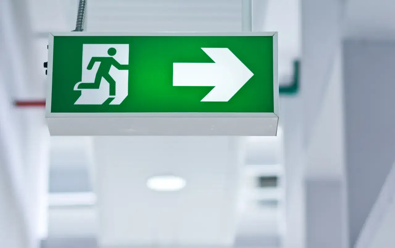 Panneau de sortie de secours vert lumineux avec une silhouette courant vers une flèche. Le baes signification est clair : une voie d'évacuation.